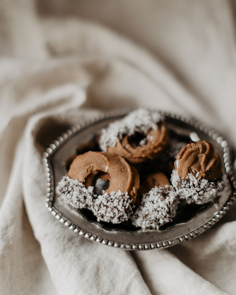 Schoko Spritzgebäck mit Schokolade-Kokosette Spitzen in silbener Schale auf beigem Geschirrtuch